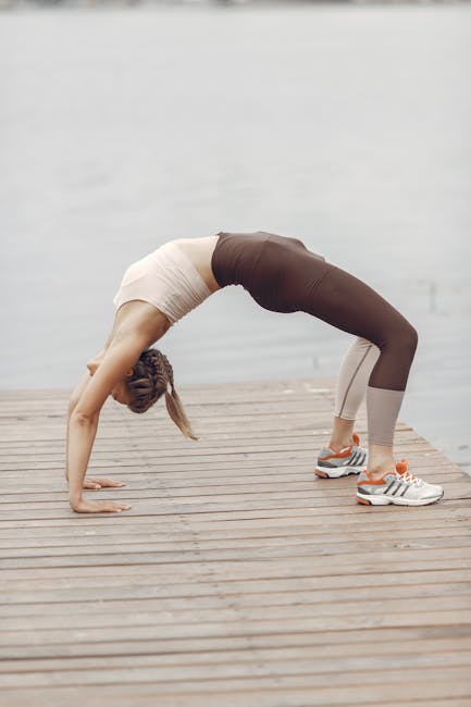 Woman meditating in a lotus yoga pose on a pier next to a tranquil lake.